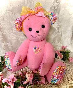 a pink teddy bear sitting on top of a table next to some flowers and leaves