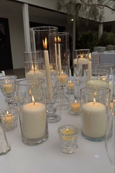 a table topped with lots of white candles and glasses filled with water on top of it