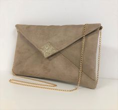 "A beige wedding clutch bag with golden sequins, in suede with a very velvety feel, with a stitched yoke on the front.  The tip of the flap is covered with gold glitter fabric. Two options are possible: WITH or WITHOUT removable shoulder chain, the choice is yours! Gold chain shoulder strap: This one is very easily removable and your bag will become a clutch! (length 120 cm) This handbag flap envelope shape, will be very trendy for your outings, a wedding, bridesmaids or a ceremony. It will easily contain your essential phone, makeup, keys, glasses, papers .... It is lined with printed cotton fabric coordinated. The very nice quality of the suede, which is also canvas, ensures a very good hold. The closing of the flap is done by a golden magnetic button. It is scratched inside \"Lesfilsdis Beige Clutch, Wedding Clutch Bag, Unique Envelopes, Beige Wedding, Clutch Bag Wedding, Tablet Bag, Wedding Clutch, Shoulder Chain, Ladies Clutch