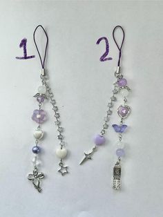 two necklaces with charms attached to them on a white surface, one is purple and the other is silver