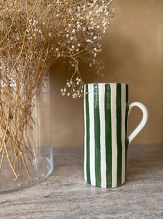 a green and white striped mug sitting next to a vase with flowers in it on a table