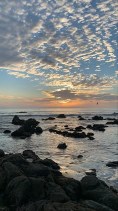 the sun is setting over the ocean and rocks