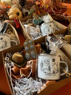 two white coffee mugs with hats and other items in boxes on an orange table