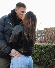 a man and woman kissing in front of a hedge