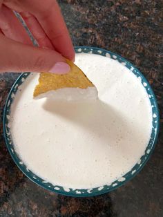 a person dipping some kind of food into a bowl with white liquid in it on a table