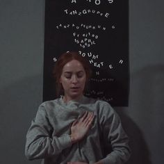 a woman standing in front of a blackboard with writing on it and her hands clasped to her chest