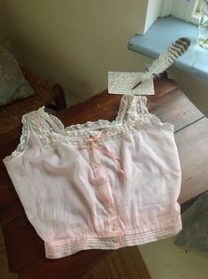 a cotton and lace camisole in a pink color with coral pink silk ribbon, and beautiful buttons. there is a little faded stain at the front ( photo 7.) in excellent condition bust 88 cm  34.5" waist 63 cm 24 3/4" Fitted Pink Top With Delicate Lace, Fitted Pink Delicate Lace Top, Pink Lace Trim Camisole In Coquette Style, Pink Lace Trim Coquette Camisole, Vintage Cotton Cami Top, Vintage Camisole Top For Daywear, Pink Lace Camisole In Coquette Style, Pink Cotton Camisole With Lace Trim, Pink Lace Coquette Camisole