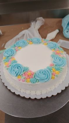 a white cake with blue frosting and colorful flowers on the top is sitting on a table