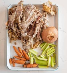 an assortment of meat and vegetables on a tray with garlic, carrots, celery