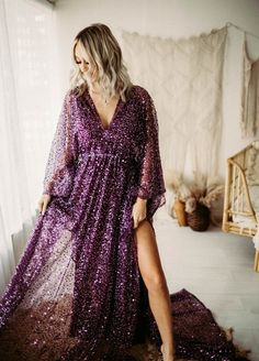 a woman wearing a purple sequin dress standing in front of a window with her legs crossed