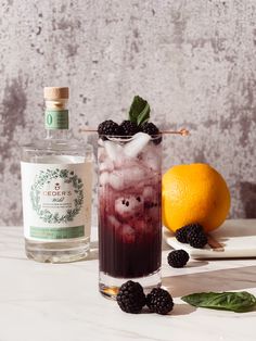 a glass filled with liquid next to an orange and blackberries on a white table