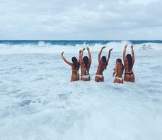 three women in bikinis are standing in the water at the beach with their arms up