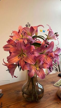 a vase filled with pink flowers sitting on top of a wooden table next to a phone