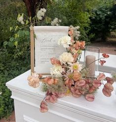 an arrangement of flowers is on top of a white table with a sign and candles