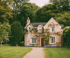 an old brick house surrounded by greenery and trees on a path leading to the front door