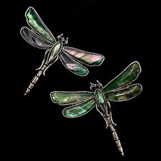 two green dragonfly brooches sitting next to each other on a black background