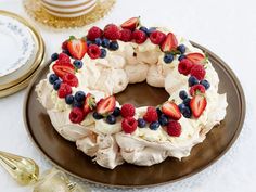 a cake decorated with berries and whipped cream on a brown plate next to goldware