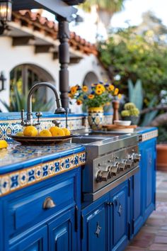 an outdoor kitchen with blue cabinets and yellow fruit on the counter top, along with potted plants