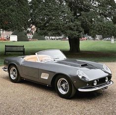 an old fashioned sports car parked in front of a park bench