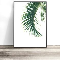 a green palm leaf print hanging on a wall next to a wooden shelf with a plant in