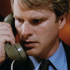 a man in a suit and tie talking on an old style telephone while wearing a necktie