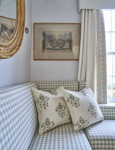 a blue and white checkered couch with pillows in front of a framed painting on the wall