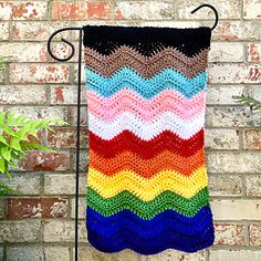 a multicolored crocheted towel hanging on a metal rack next to a brick wall