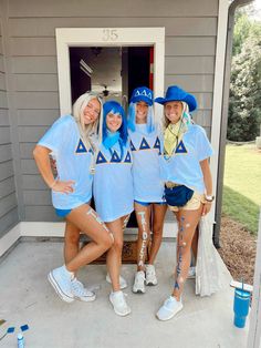 three women in blue shirts and white shorts posing for a photo on the front porch