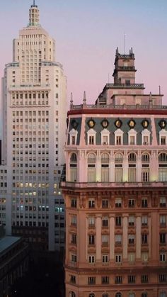 an old building in the middle of a city with tall buildings behind it at dusk