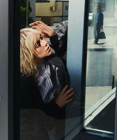 a woman leaning against the side of a building with her hand on her head and looking out