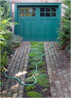 a green garage door with a hose connected to the side walk in front of it