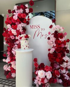 a wedding cake surrounded by red and pink flowers in front of a miss to mrs sign