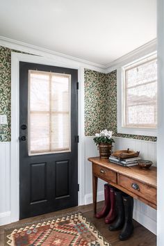 the entryway is decorated with floral wallpaper and an antique wooden table, along with two well - worn rubber boots