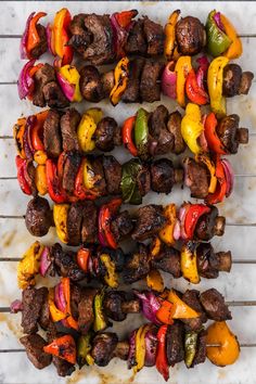 several skewers of meat and vegetables on a white table top with grate