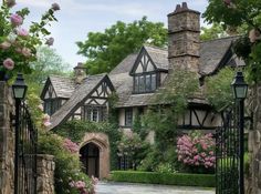 an old style house is surrounded by flowers and greenery in front of the gate