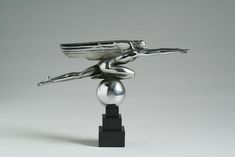 a silver statue is on top of a black stand with a ball in front of it