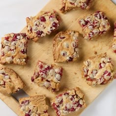 a wooden cutting board topped with cookies and cranberry scones on top of a white table