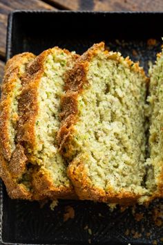 a loaf of zucchini bread cut in half on a black tray next to a wooden table