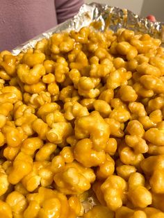 a person holding a tray full of caramel coated popcorn kernels in their hands