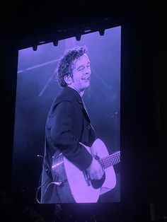 the man is playing his guitar in front of a large screen with an image of him on it