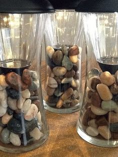 three glass vases filled with rocks on top of a wooden table next to each other