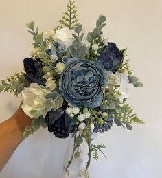 a bouquet of blue flowers and greenery on a white wall with a hand holding it