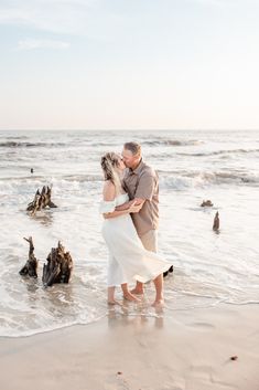 a man and woman kissing on the beach with seagulls in the water behind them