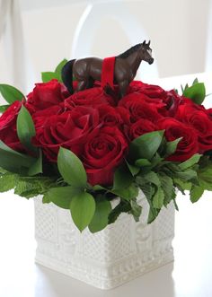 a white vase filled with red roses and a horse figurine sitting on top of it