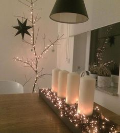 some candles are sitting on a table near a christmas tree with lights around it and a black star hanging from the ceiling