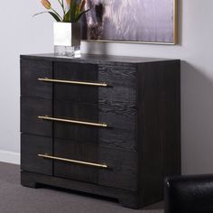 a black dresser with three drawers and a vase on top, in front of a white wall