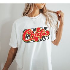 You will love this super cute and cozy Kansas City Chiefs shirt! This is a unisex fit t-shirt, made with direct to film transfer, no vinyl or sublimation is used.  T-shirts are comfort colors soft washed garment-dyed tees, renowned for their softness, comfort, and durability. Made with 100% ring-spun cotton, and sure to make an excellent choice for comfortable daily wear. T-shirts have double needle stitching throughout, sewn in twill label, and ribbed collar.  In order to provide the most color choices, sweatshirts in Pepper and Ivory are made using Comfort Colors 100% soft ring-spun cotton, while sweatshirts in white, black, grey, red, and sand are made using Gildan Cozy Feel, 50% cotton 50% poly blend. Both have a ribbed collar and relaxed fit and will make a great addition to your game Kc Chiefs Shirts Vinyl, White Cotton Sublimation T-shirt With Funny Print, Pop Culture Short Sleeve Shirt With Letter Print, White Pop Culture Shirt With Letter Print, Casual Cotton Sublimation T-shirt With Funny Print, Casual Cotton Sublimation Design With Funny Print, Pop Culture Relaxed Fit Shirt With Letter Print, Funny Print Graphic Tee, White Shirt With Sublimation Print In Pop Culture Style