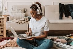 a woman is sitting on the floor with her laptop and headphones in her ears