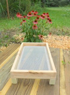 a wooden table sitting on top of a wooden deck next to a flower pot filled with red flowers