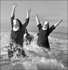 black and white photograph of two women in the ocean with their arms up, both wearing nun costumes